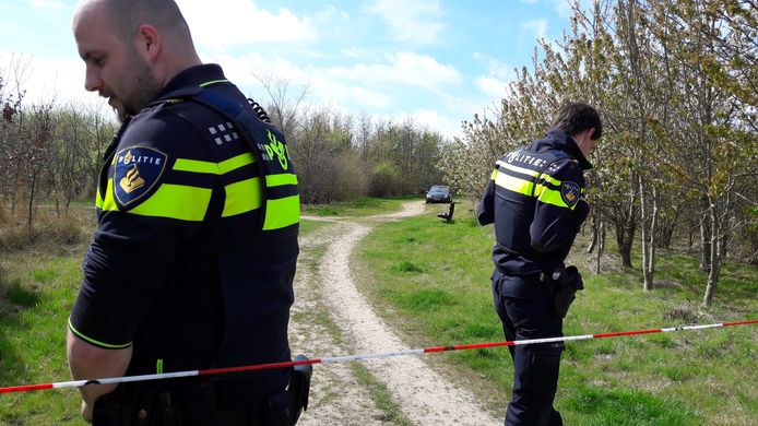 Politie-agenten staan vlakbij de plek waar de man en vrouw dood werden gevonden. In de verte de Mercedes die werd aangetroffen.