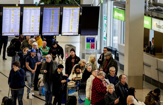 Reizigers op Schiphol kijken naar schermen voor hun reis. Alle vluchten zijn door de westerstorm op Schiphol geannuleerd.