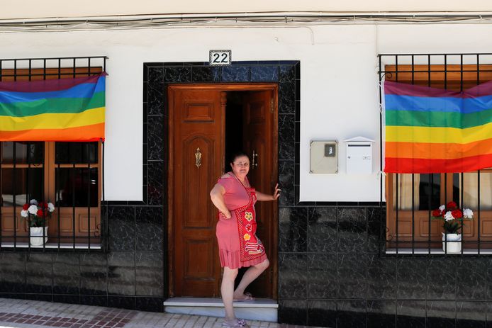 Een vrouw poseert bij enkele regenboogvlaggen voor haar huis.