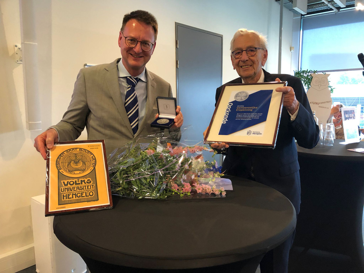 Voorzitter Frans Tillemans (rechts) ontving vrijdag van wethouder Claudio Bruggink de erepenning vanwege het 110-jarig bestaan van de Volksuniversiteit Hengelo. Met daarbij, ingelijst en wel, de voorkant van het eerste programmaboekje.