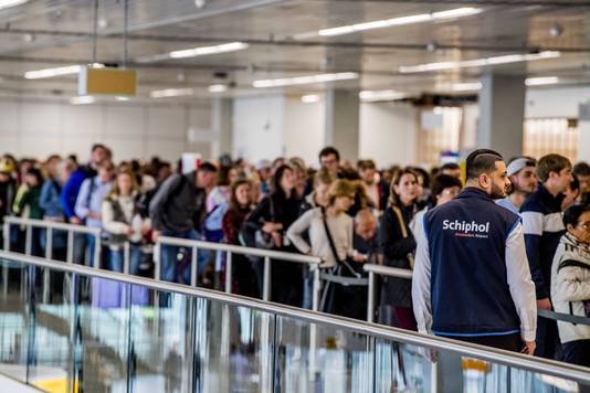 Reizigers wachten in rijen voor de bagagecontrole op luchthaven Schiphol.