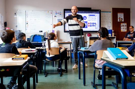 Een leraar laat in de klas aan basisschoolleerlingen zien wat de coronamaatregelen zijn. 