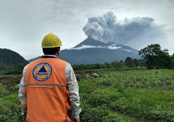 Een medewerker van de nationale rampenbestrijding kijkt naar de uitbarsting van de Fuego-vulkaan op de achtergrond.
