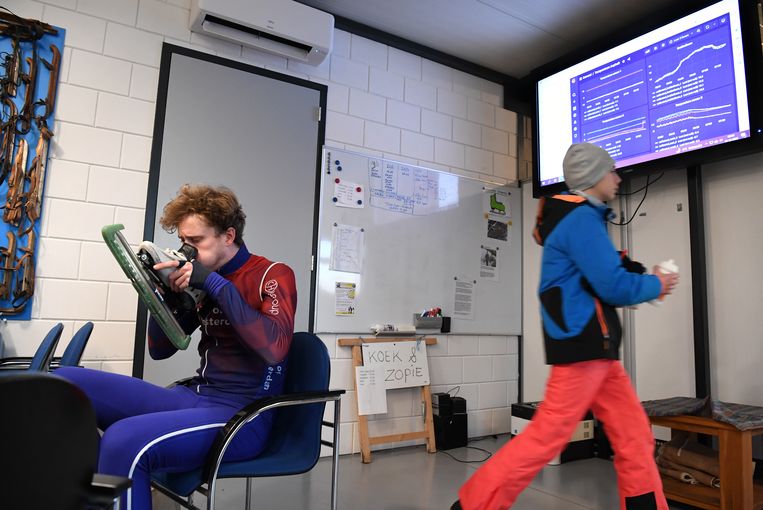 Bart Vreugdenhil blaast zijn schaatsen warm in het clubgebouw van de ijsvereniging. Op het scherm in de achtergrond informatie over de ijsvloer en het weer. Beeld  Marcel van den Bergh / de Volkskrant