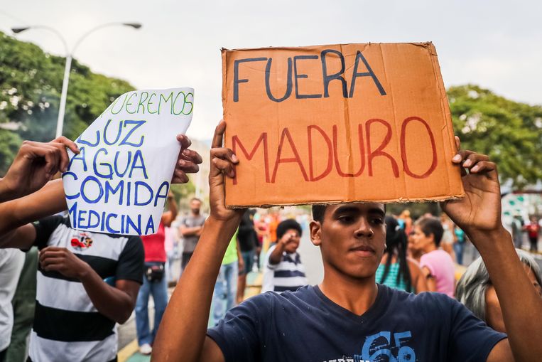 Mensen protesteren tegen het gebrek aan drinkwater en elektriciteit in Venezuela. ‘We willen licht, water, eten en medicijnen’, staat op het bord linksachter. De man rechtsvoor heeft een simpele boodschap: ‘Maduro Buiten’. Beeld EPA