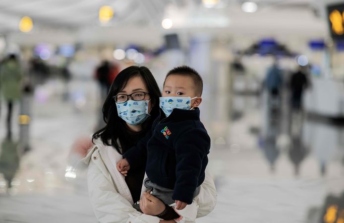 Beschermd door een mondkapje checken een vrouw en een kind in op het vliegveld van Beijing.