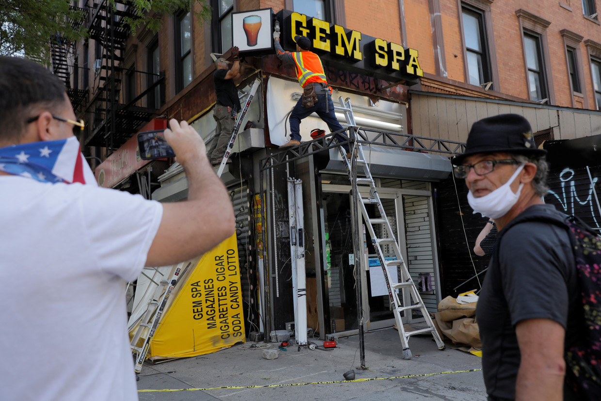 Voorbijgangers kijken toe als het uithangbord wordt verwijderd van een winkel in Manhattan die failliet is gegaan door de lockdown. Beeld REUTERS