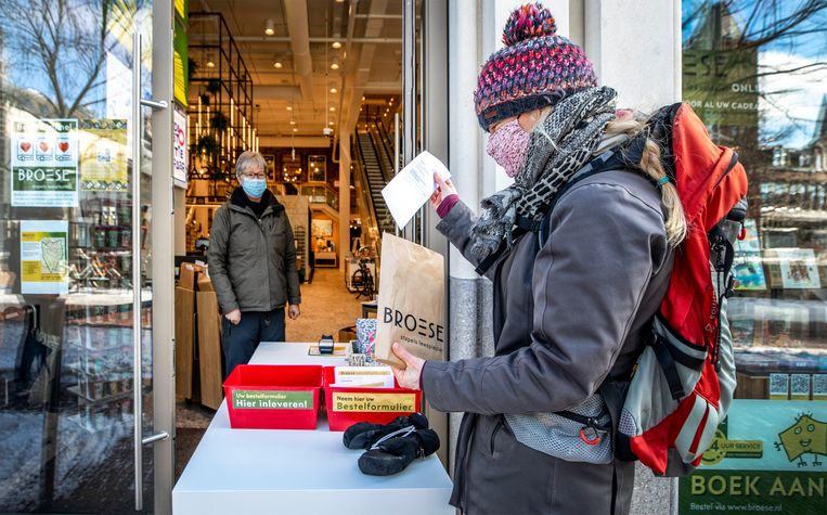 Een klant haalt een pakje af bij boekhandel Broese in hartje Utrecht. Binnen staat een medewerker die alle voorbijgangers begroet. Beeld Raymond Rutting / de Volkskrant