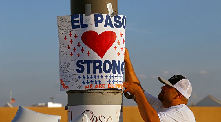 Een man hangt een poster op bij een monument voor de slachtoffers van de schietpartij in El Paso. Beeld EPA