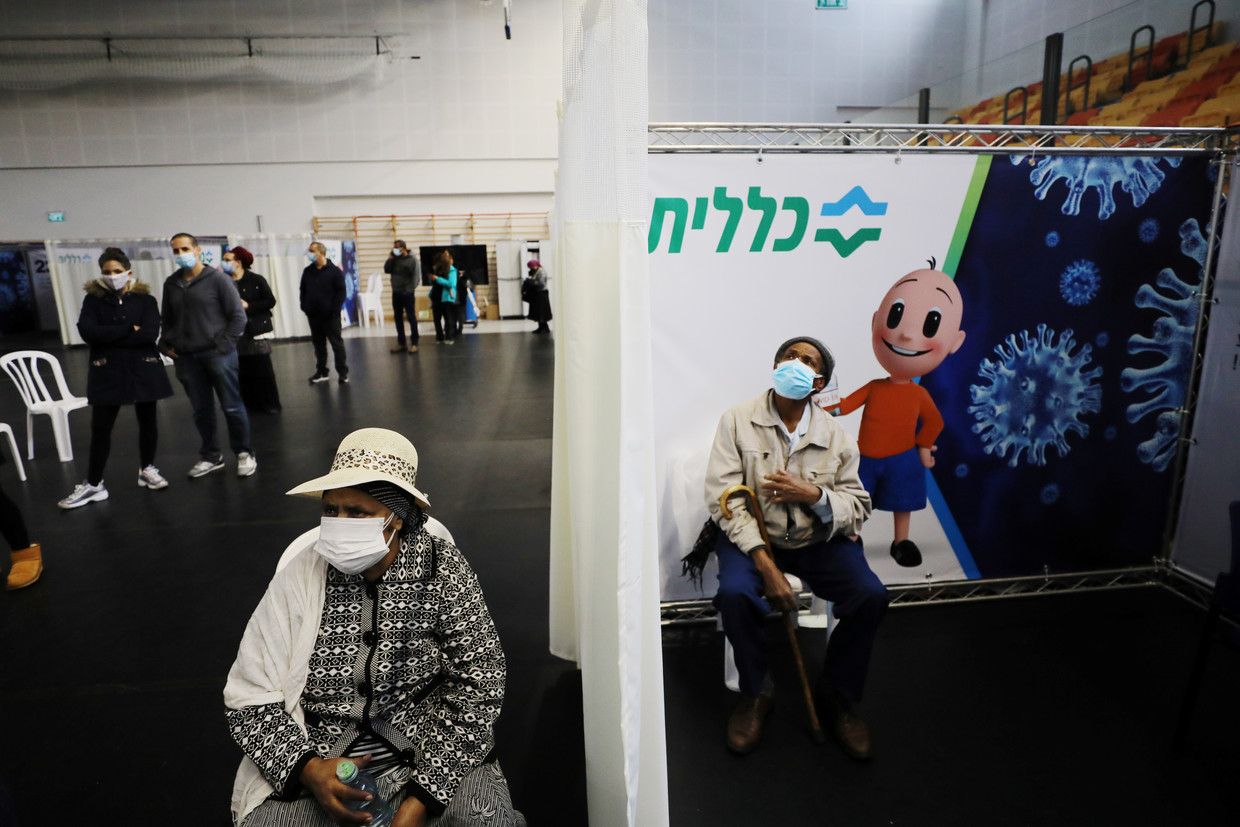 Een vrouw wacht op haar vaccinatie, een ander zit even bij te komen na het hebben gekregen van de prik in het Israëlische Petah Tikva.  Beeld REUTERS