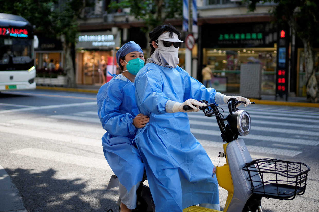 Vrouwen in beschermende kledij rijden op een elektrische scooter door de straten van Shanghai. Beeld REUTERS