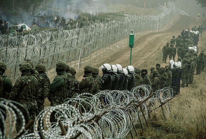 Poolse militairen en agenten bij de grens met Belarus waar aan de andere kant van het hek migranten wachten