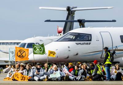 Honderden klimaatactivisten blokkeren privéjets op Schiphol, sommigen zitten vastgeketend aan vliegtuig