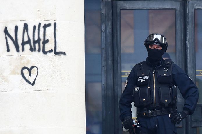 A cop stands next to a wall with Nahel's name written in Nantes.