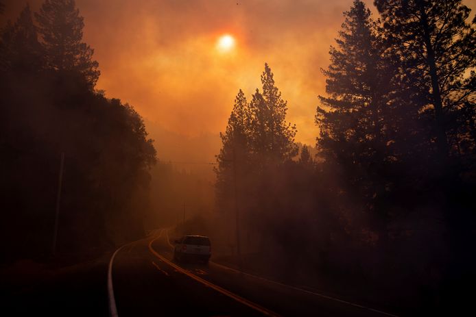Een auto rijdt door de rook van de branden heen.