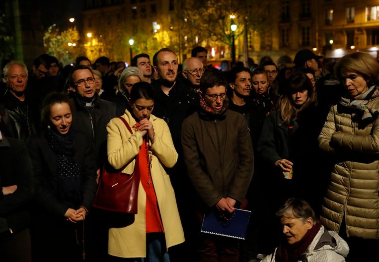 Mensen in Parijs hebben zich verzameld om te bidden en stil te staan bij de kerk die in brand staat. Beeld AP