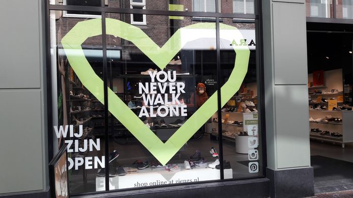 Oproep tot elkaar steunen in de Ketelstraat in Arnhem: You Never Walk Alone op de etalage van de weer geopend schoenenzaak Ziengs.