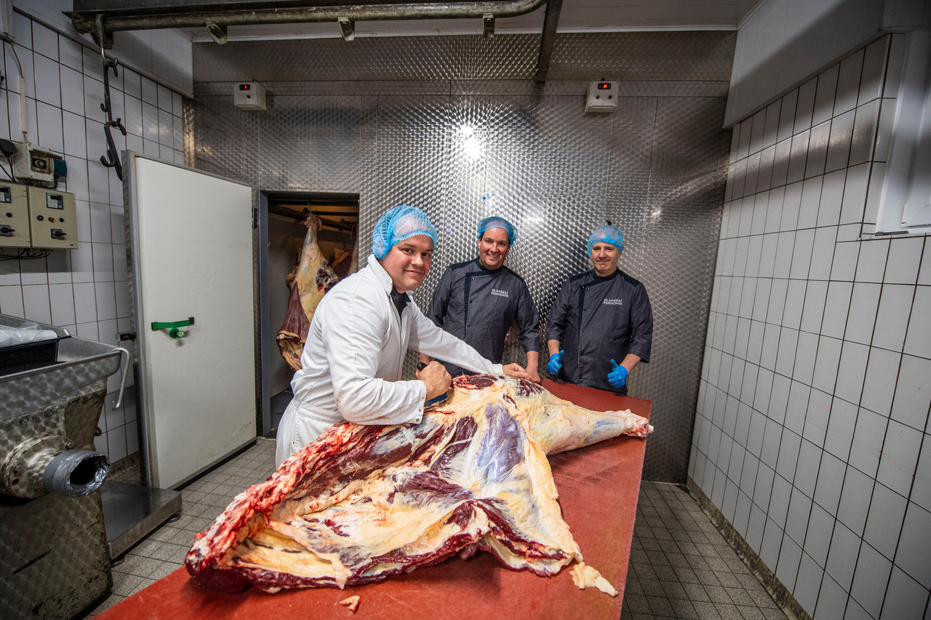 Gerben, Eric en Gerdwin Pennings nemen een achterbeen van een rund onder handen in hun slagerij.