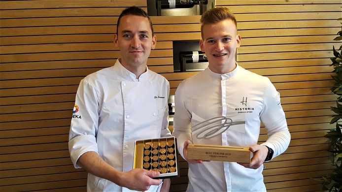 Leerkracht Christof Lauwers en oud-leerling Yannick Haast tonen de praline en trofee.