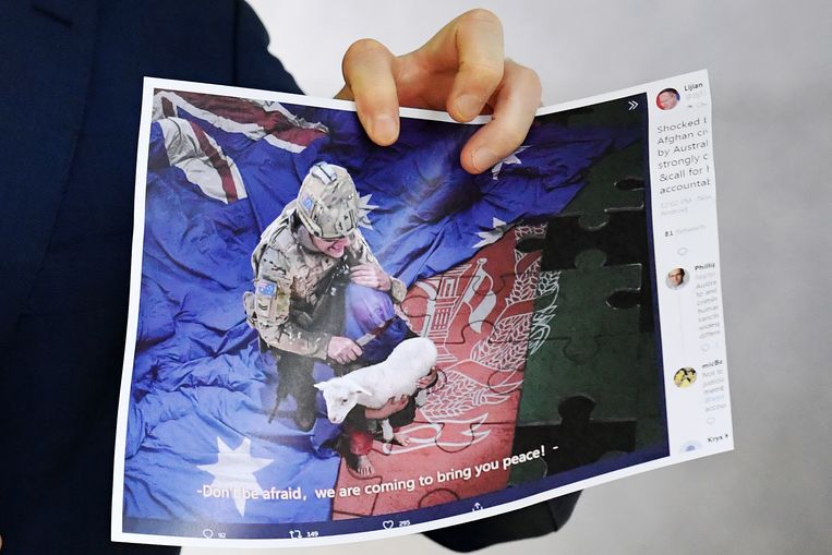 Een journalist houdt een kopie van de foto vast die topdiplomaat Zhao Lijian deze maandag twitterde. De gemanipuleerde afbeelding toont een Australische militair die aanstalten maakt een Afghaans kindje de keel af te snijden.  Beeld EPA
