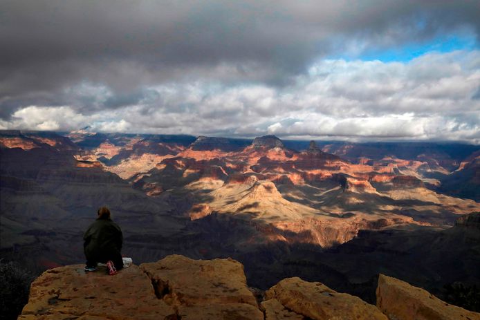 Een vrouw zit dicht bij de rand van een klif aan de zuidkant van de Grand Canyon.