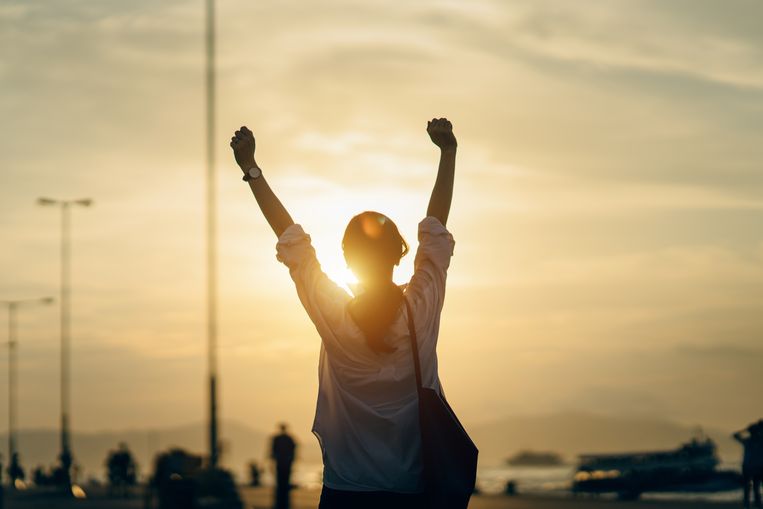 Young woman relaxing with hands in the air by the pier and enjoying the beautiful sunset and warmth of sunlight Beeld Getty Images