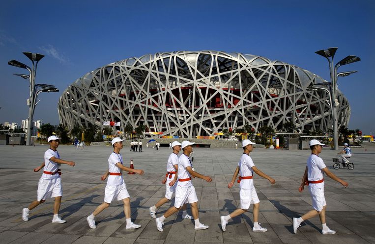 Vrijwilligers lopen op het plein voor het Olympisch stadion in Peking, in de volksmond het Vogelnest genoemd. Beeld ANP