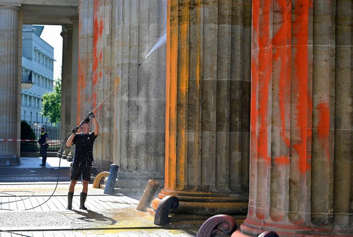 Immagine per chiarimenti.  Un uomo rimuove la vernice da un pilastro della Porta di Brandeburgo, simbolo di Berlino.