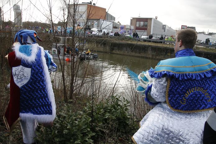 Enkele carnavalsvierders kijken toe hoe hulpverleners de Dender met een sonarboot doorzoeken.