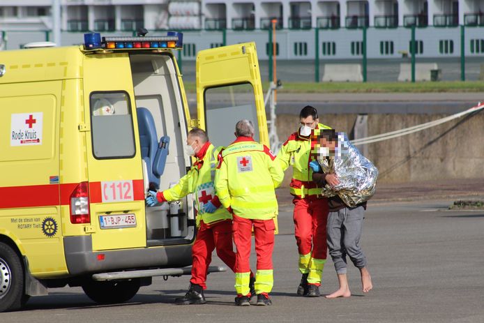 Een transmigrant kreeg een dekentje van de hulpdiensten en wordt hier met de ambulance naar het ziekenhuis gebracht