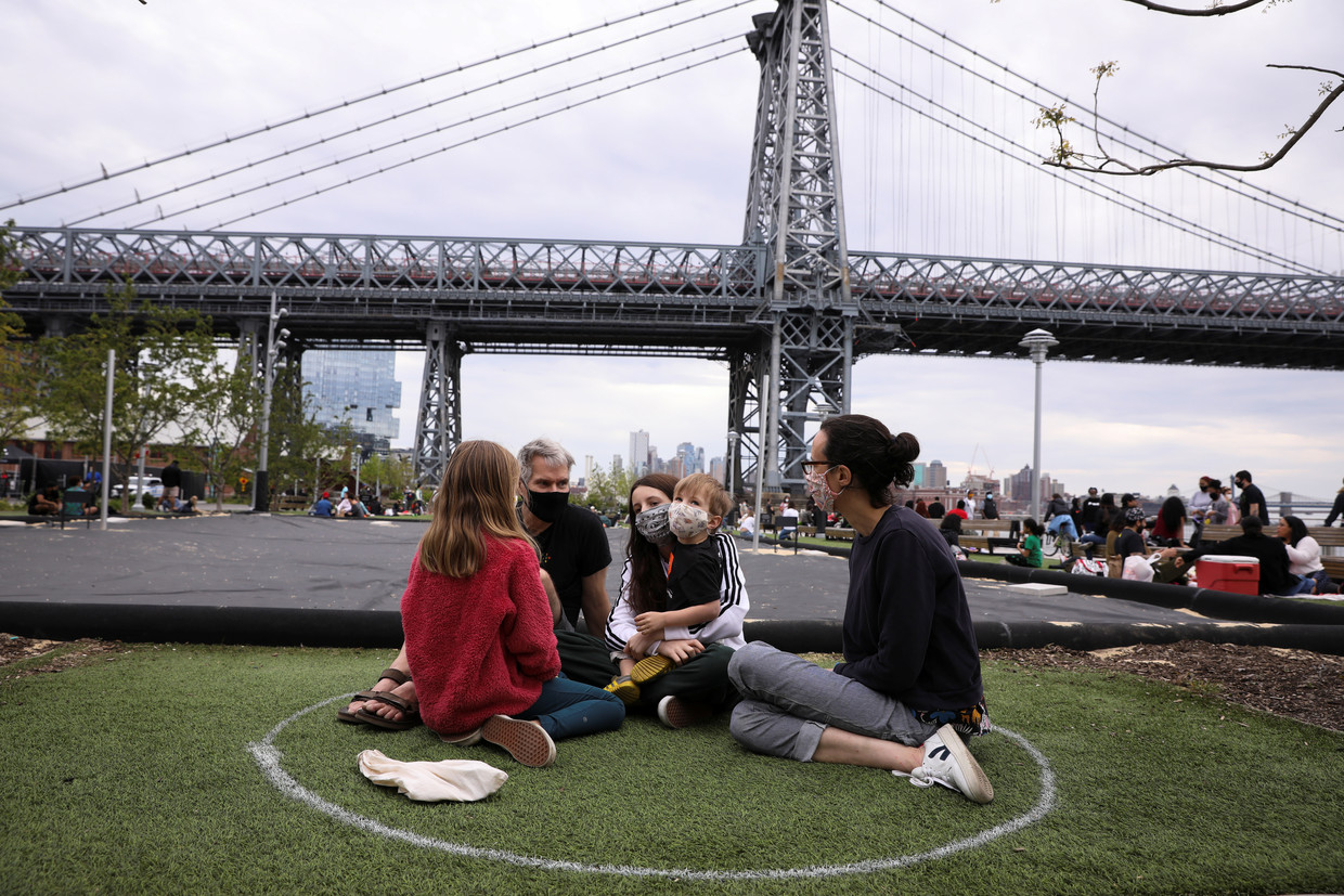 Een gezin in het Domino Park in New York, waar cirkels op het gras staan getekend om afstand te kunnen houden.  Beeld REUTERS