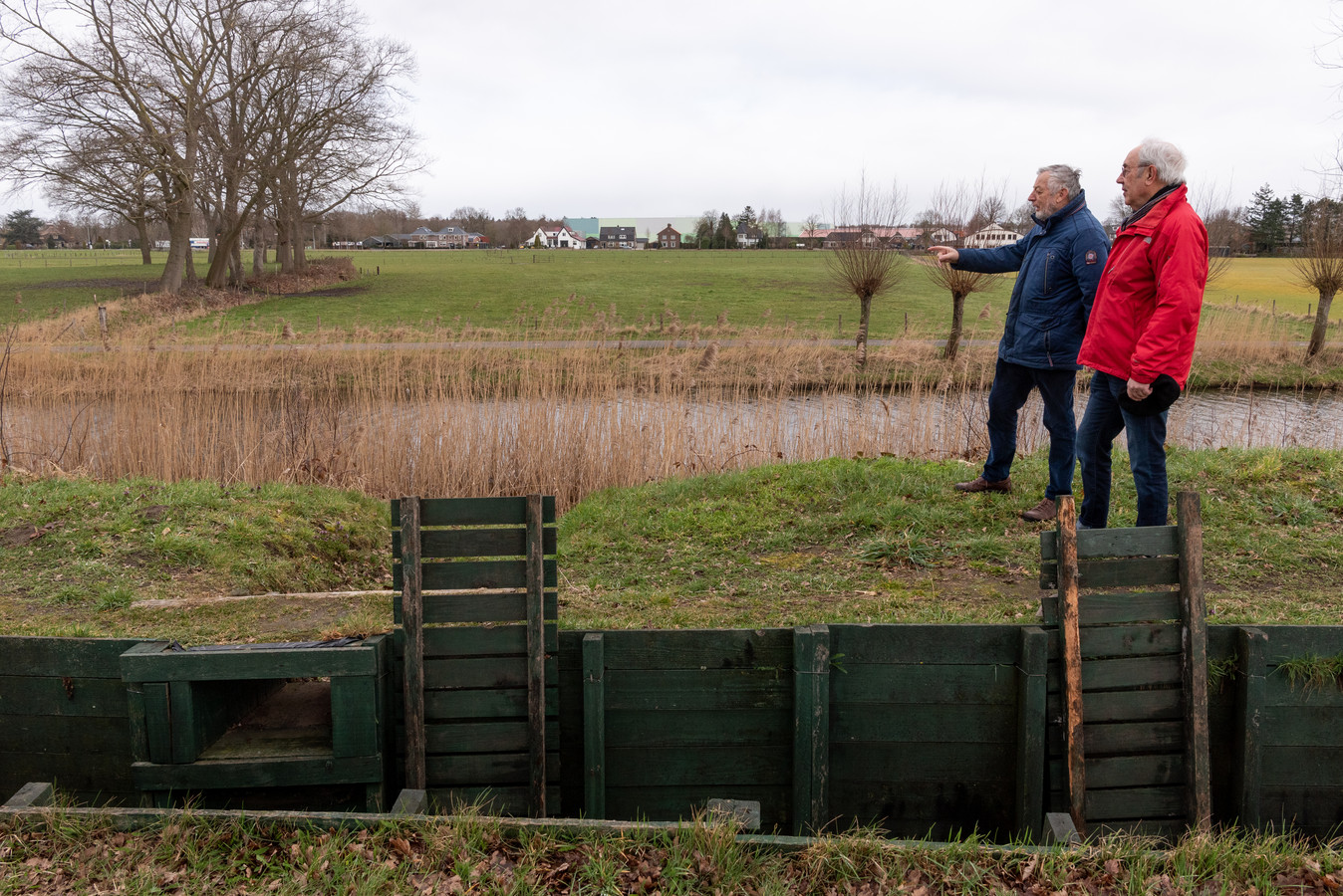 Buurtbewoners Nico de Haan (links) en Jan Ruijgrok, in de winter gefotografeerd, staan bij de loopgraven van de Grebbelinie. Op het weiland aan de overkant van de sloot komt een groot distributiecentrum van Modiform, is het plan. Op de achtergrond de dorpsrand van Scherpenzeel.