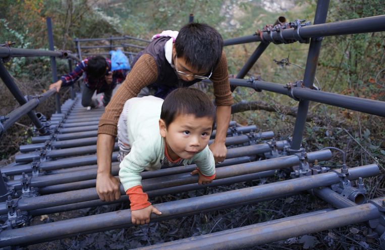 Een leraar helpt een peuter een ladder op in de prefectuur van Liangshan, Sichuan.  Beeld Getty