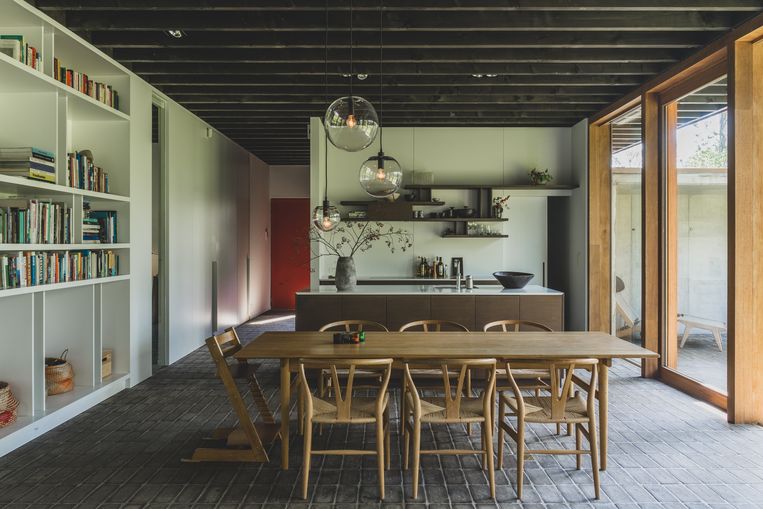 Een van de weinige kleuraccenten in de woning is de rode voordeur. Voor de inrichting kozen Peter en Alexandra voor sobere designklassiekers zoals deze tafel en stoelen van Hans Wegner.  Beeld Hannelore Veelaert