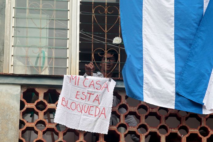 De Cubaanse toneelschrijver en dissident Yunior García Aguilera aan het raam van zijn huis in Havana, Cuba. Hij houdt een spandoek vast waarop staat "Mijn huis is omsingeld".