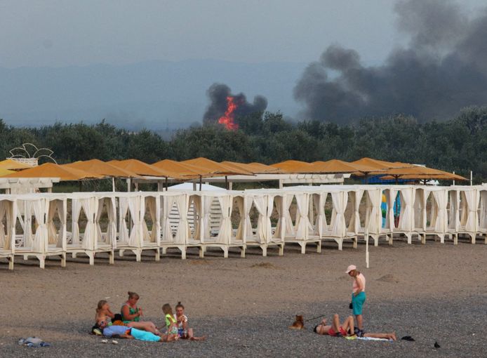 Mensen relazen op het strand terwijl op de achtergrond explosies op een Russische militaire basis op de Krim te zien zijn.