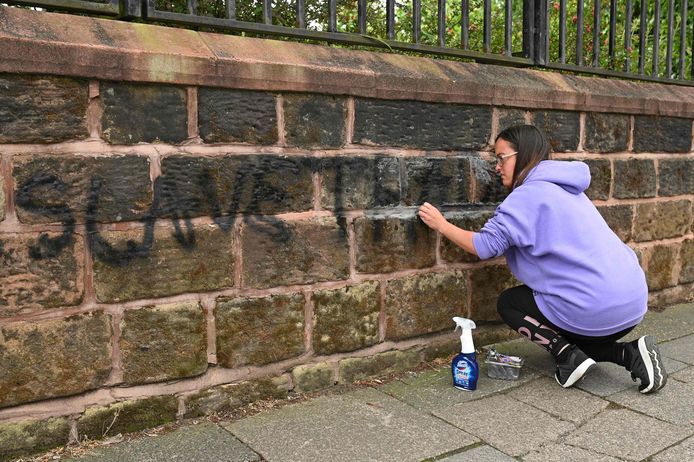 Een buurtbewoonster probeert de graffiti weg te poetsen.