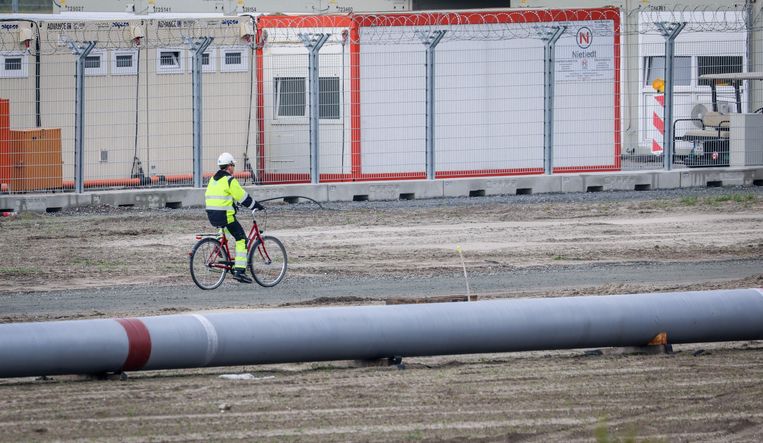Een medewerker fietst over het terrein langs een buis op het bouwterrein van de Uniper LNG-terminal in het Duitse Wilhelmshaven. Beeld AFP
