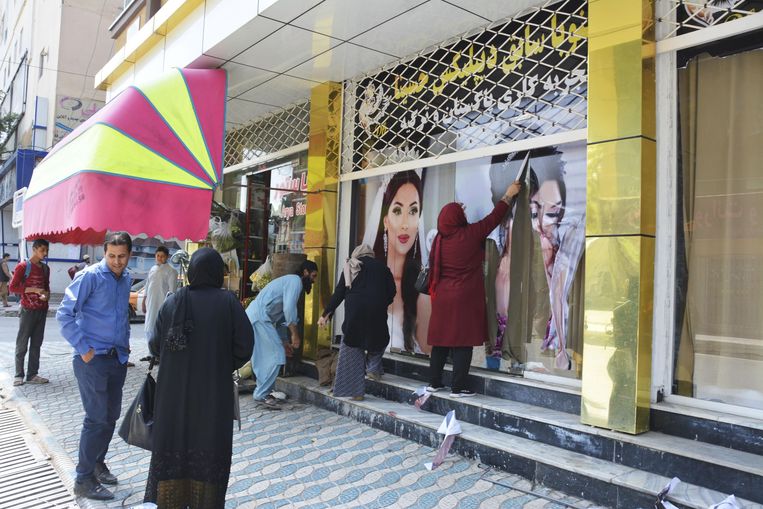 Medewerkers van een schoonheidssalon in Kaboel verwijderen afbeeldingen van vrouwen van de gevel. Beeld BELGAIMAGE