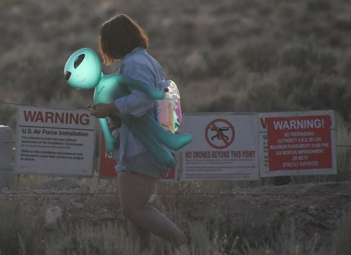 Een vrouw loopt met een plastic alien op de arm bij het hek van Area 51, een geheim militair complex in de Nevada-woestijn in de VS waar volgens ‘believers’ ufo’s worden nagebouwd en misschien zelfs de overblijfselen liggen van aliens die in 1947 zouden zijn neergestort. Archiefbeeld.