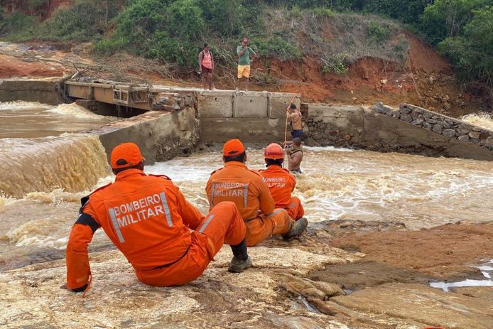 Brandweermannen helpen inwoners met het oversteken van de rivier nadat de brug is ingestort door de zware regenval.