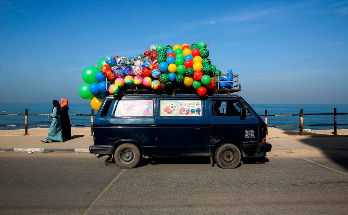 Een minibusje met kleurige ballen op het dak, rijdt langs het strand van Gaza City. Foto Mohammed Abed