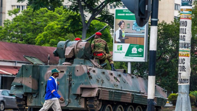 Een inwoner van de Zimbabwaanse hoofdstad Harare loopt woensdag langs een pantserwagen op een kruispunt. Het leger heeft de macht in het land overgenomen. Beeld afp