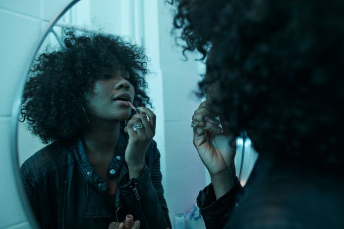 Zwarte vrouw maakt zich op in de spiegel.