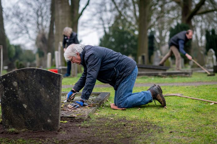 Geknield naast een graf schraapt Simon Schutte met een plamuurmes het mos van een grafzerk op de monumentale begraafplaats aan de Hengelosestraat in Oldenzaal.