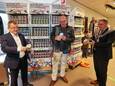Wethouder Hans van de Looij (links) en burgemeester Marcel Delhez (rechts) nemen elk een door  kunstenaar Jean-Paul Marsman (midden) ontworpen Veldhoven 100-koffiekopje in ontvangst in de supermarkt van André en Joyce van Reijen. Klanten kunnen de komende tijd voor de kopjes sparen.