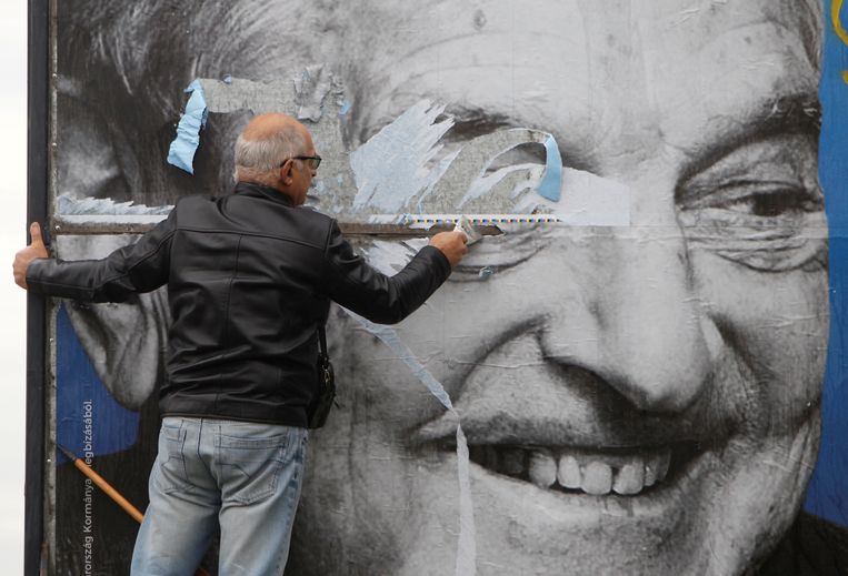Een activist van een van de Hongaarse oppositiepartijen schraapt een poster weg met daarop een negatieve uitlating over George Soros door de partij van Orbán. Beeld REUTERS