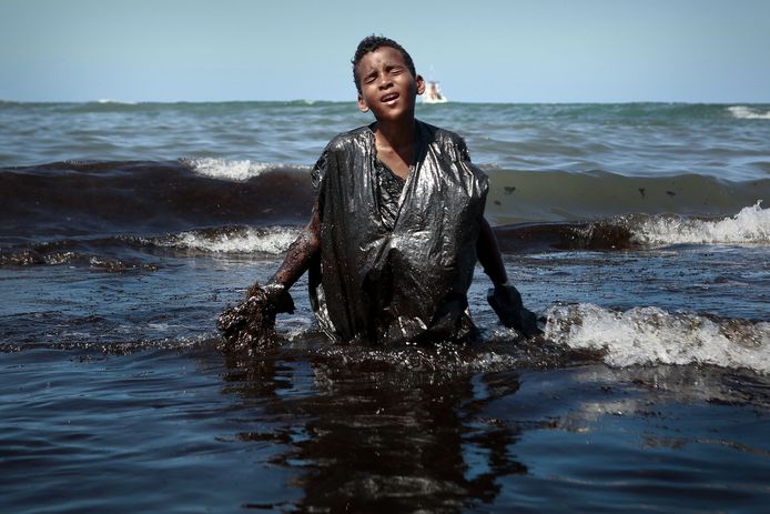 Een jongen probeert vrijwel onbeschermd olie uit zee te verwijderen aan de kust bij Cabo de Santo Agostinho in de deelstaat Pernambuco in het noordoosten van Brazilië.