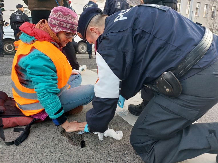 Een politieagent probeert een klimaatactivist los te wrikken die zich met lijm aan de weg heeft vastgeplakt. Beeld Anne ter Rele