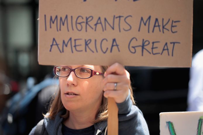 In Chicago houdt een demonstrant een bord omhoog met de tekst 'Immigranten Maken Amerika Groot', een slimme twist op Trumps verkiezingsslogan.